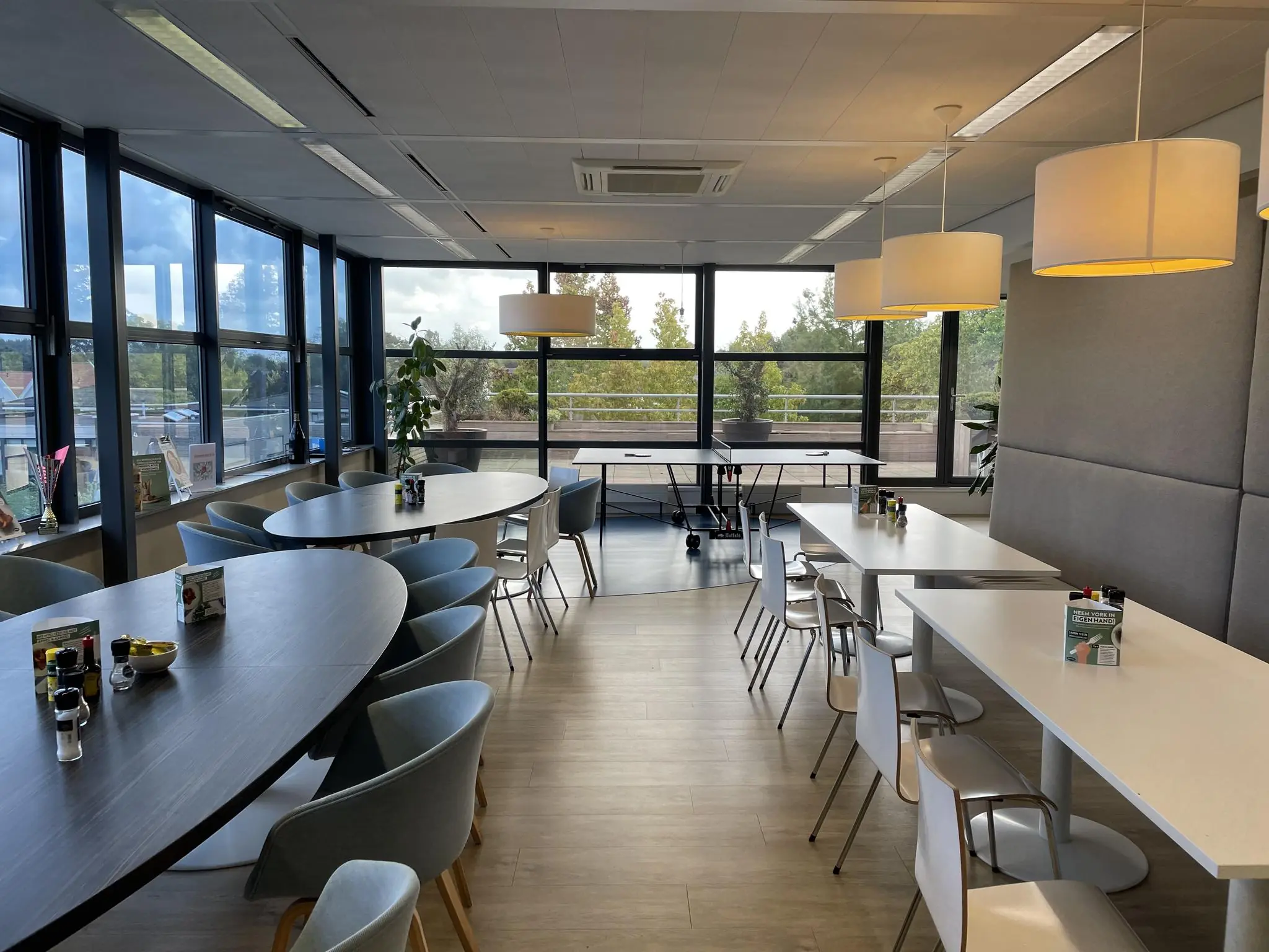 Moderne en lichte kantineruimte aan de Jan Leentvaarlaan met zitplaatsen, grote ramen en een tafeltennistafel.